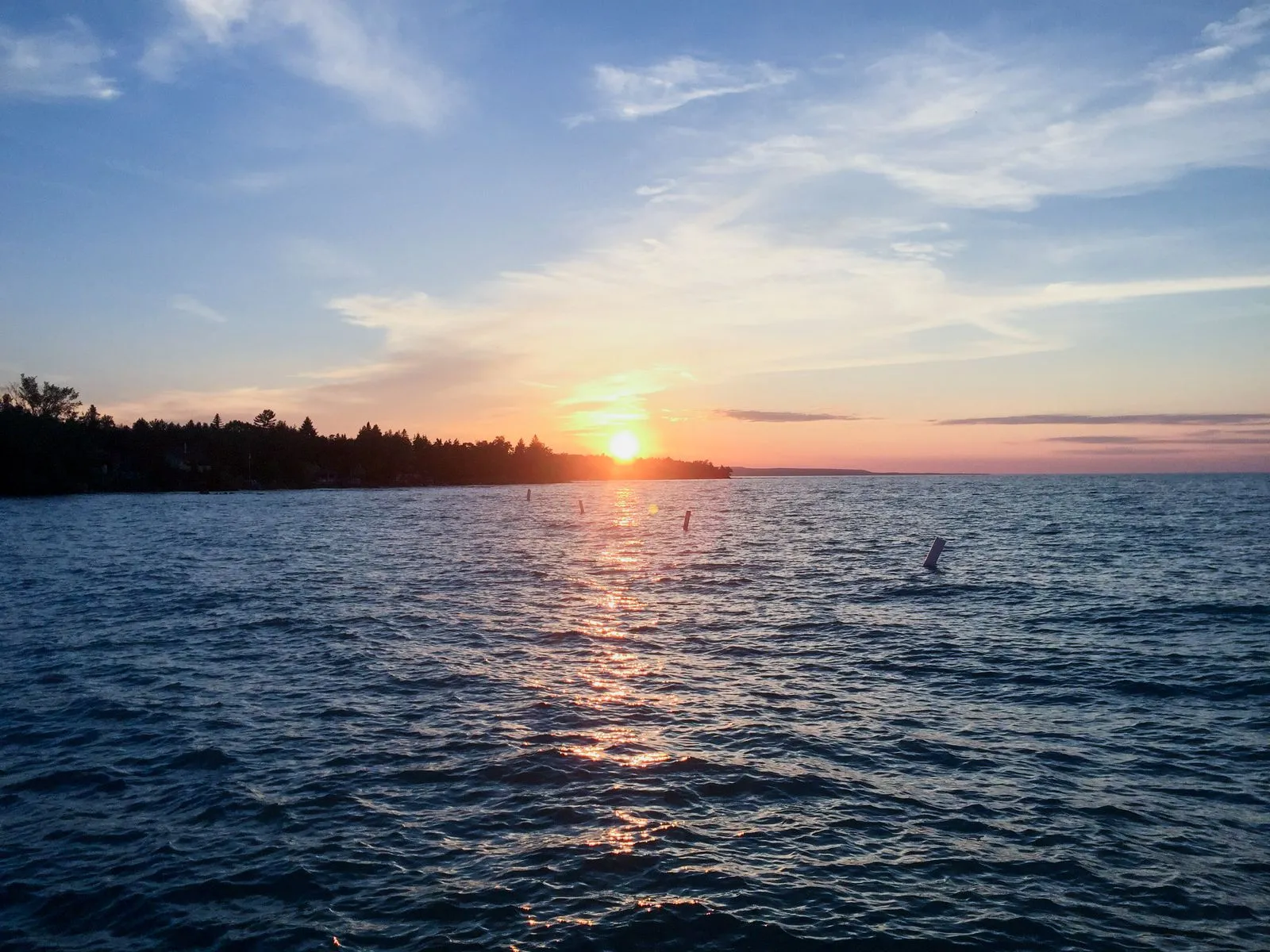 Gold sunset light on the water of a wide bay with swim buoys in the foreground