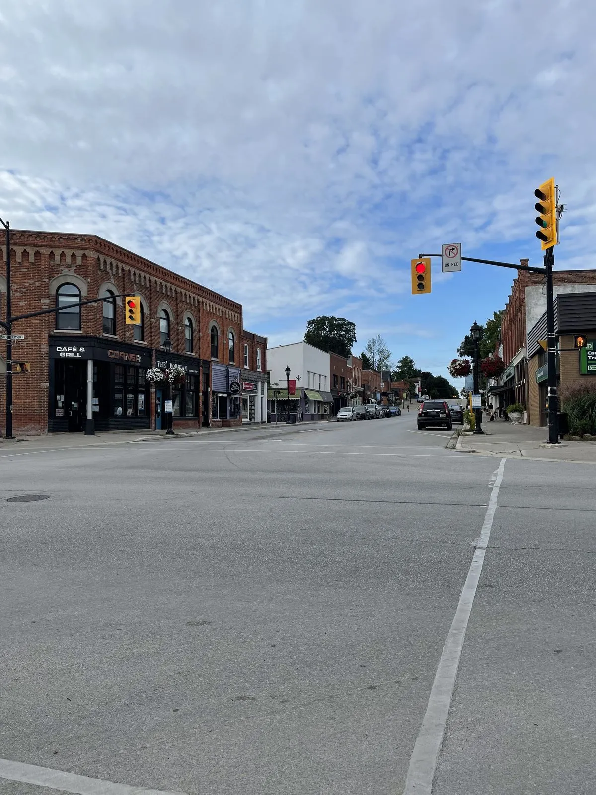 A small-town main street corner with brick storefronts and hanging flower baskets in summer