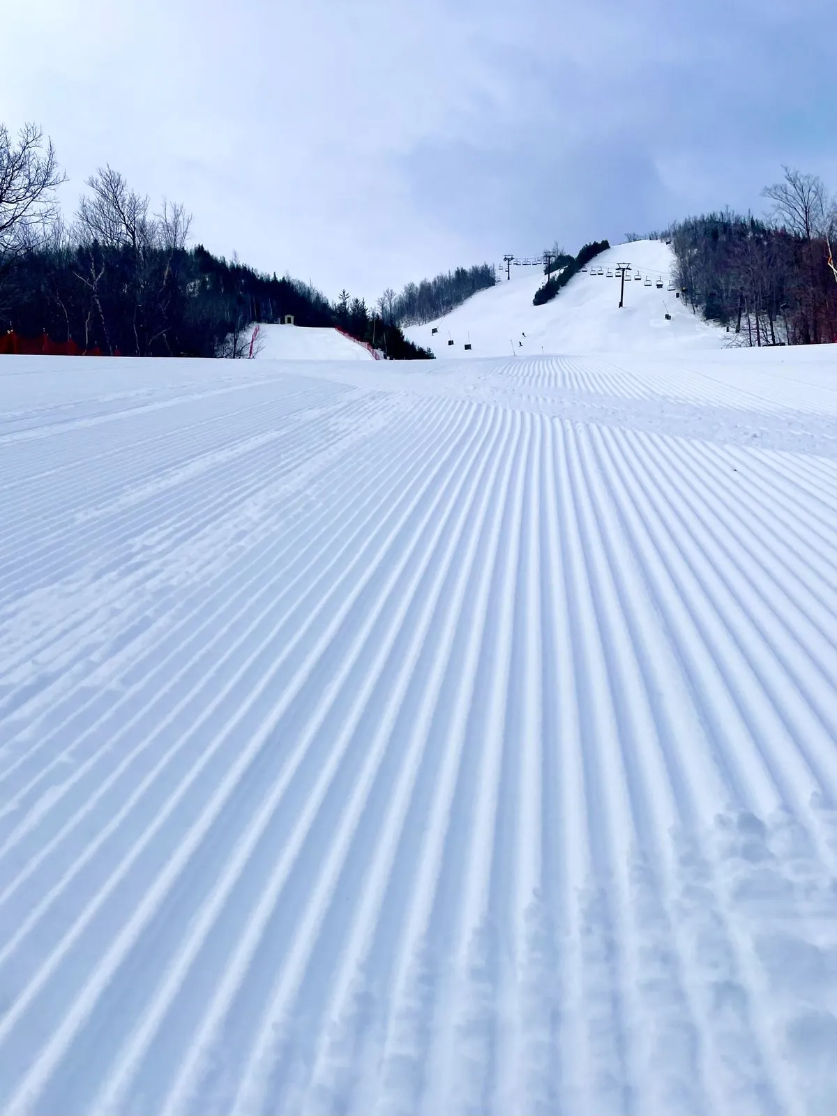Fresh corduroy on a groomed ski run with lifts on the ridge above
