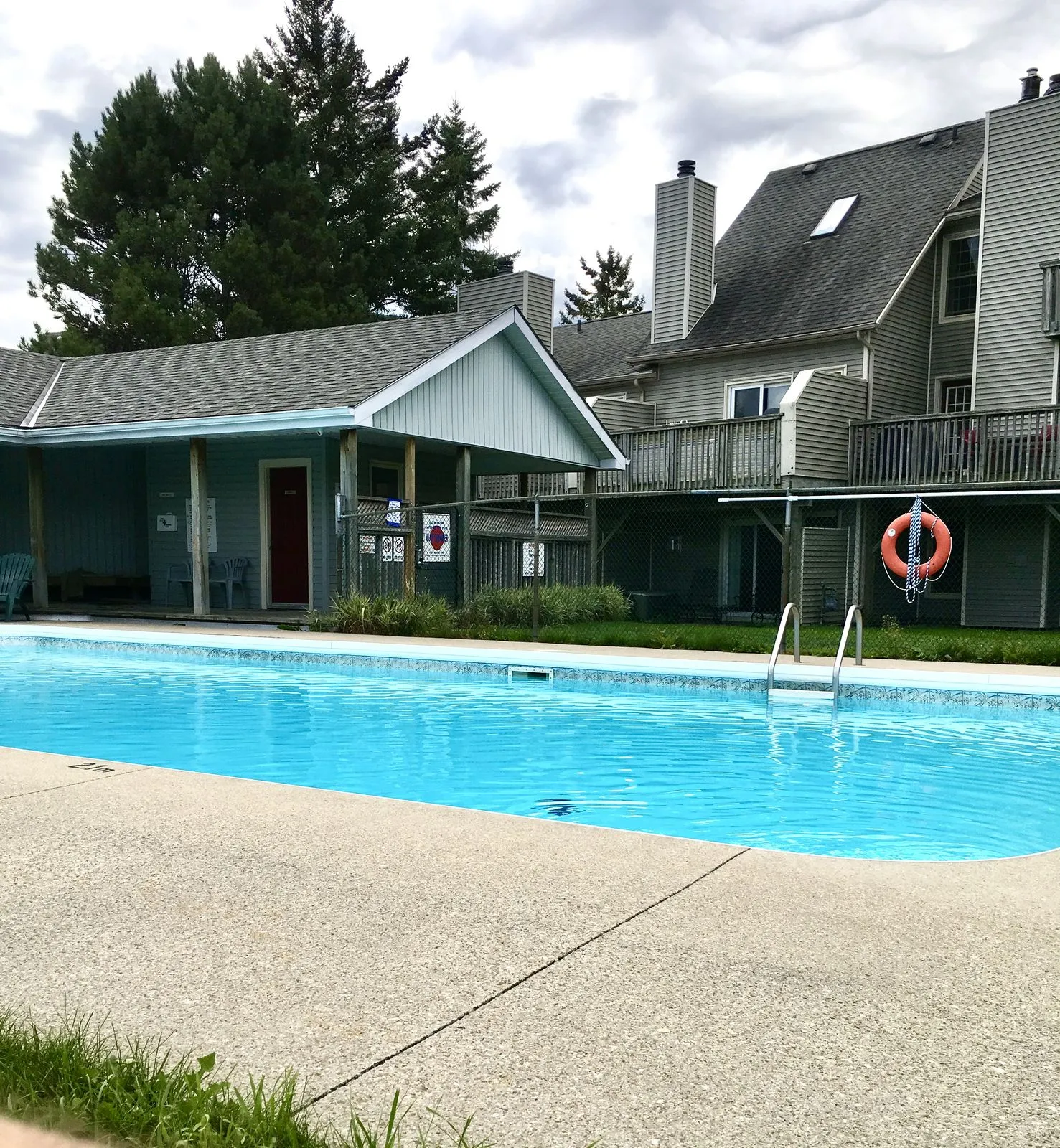 An outdoor pool with bright water, a pool house and condominium gables behind